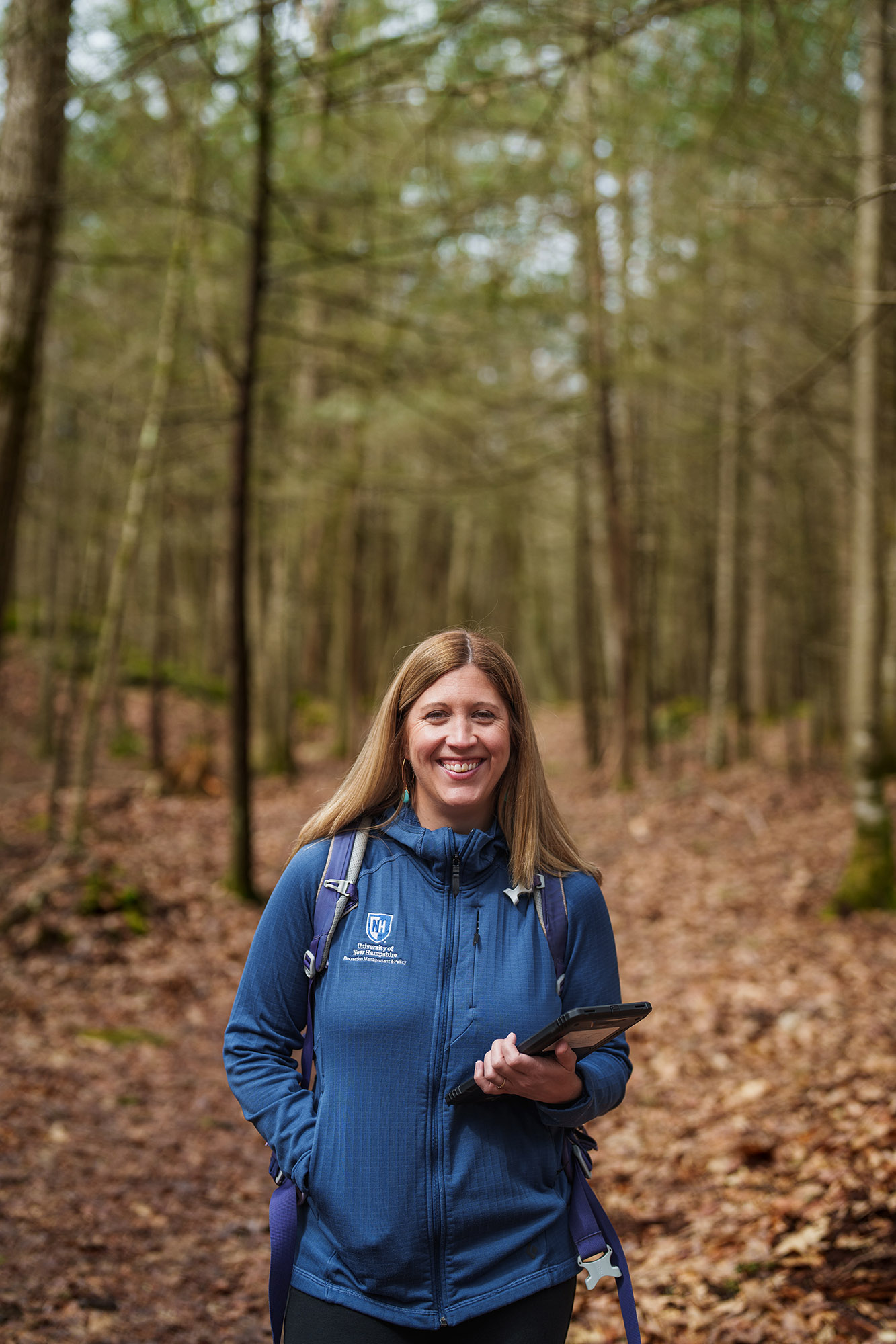 Lauren Ferguson smiling on a forest trail holding a tablet, wearing a UNH jacket