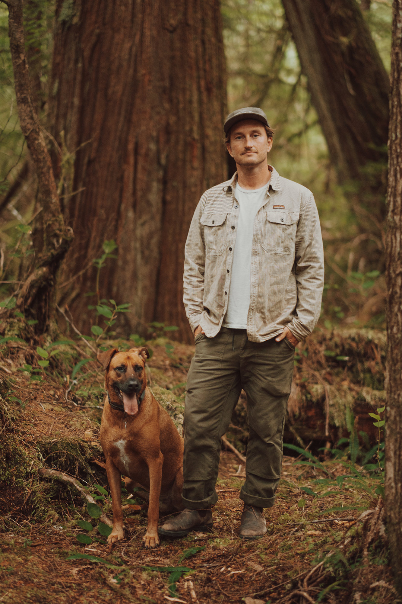 Ross Reid standing in old-growth coastal rainforest with his dog Pintxo at his side
