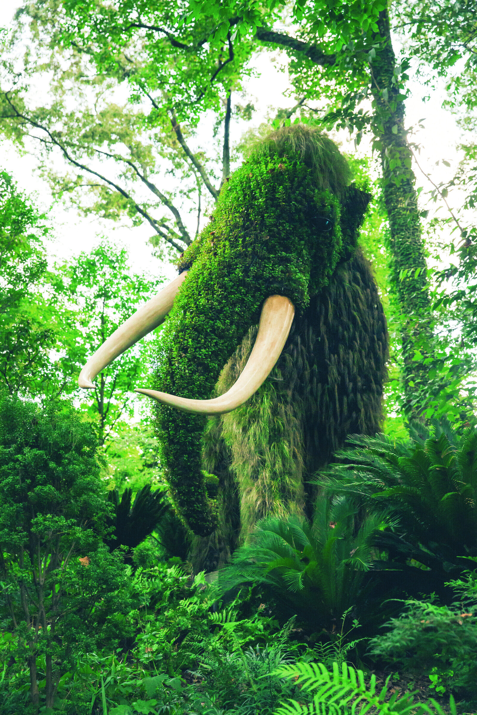 Moss-covered mammoth sculpture in a forest