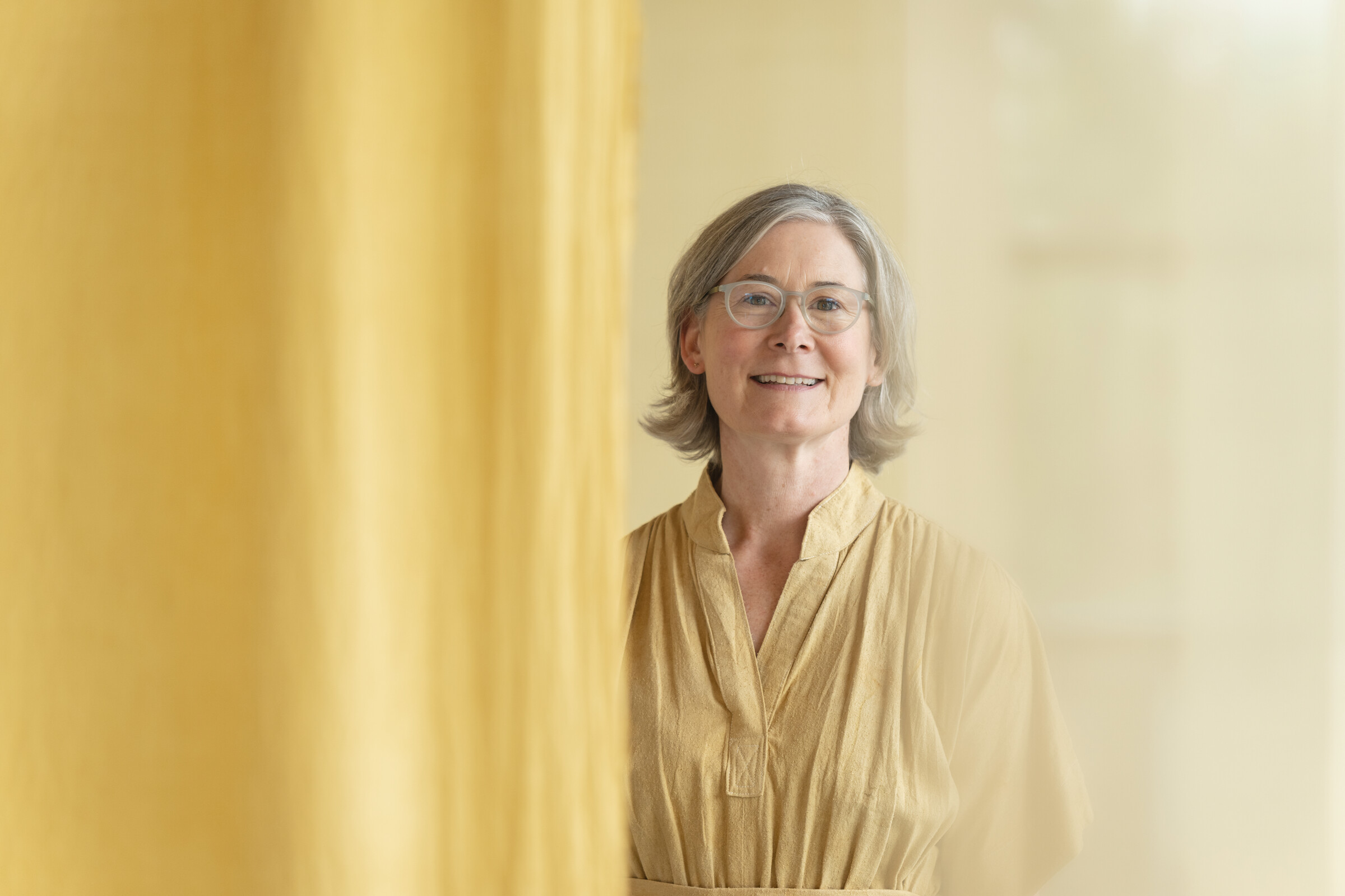 Julie Beeler smiling in front of a golden-yellow curtain